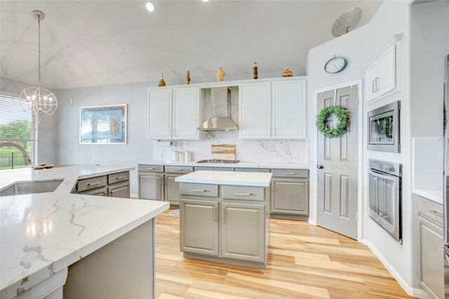 kitchen with wall chimney range hood, gray cabinets, a center island, a sink, and stainless steel appliances