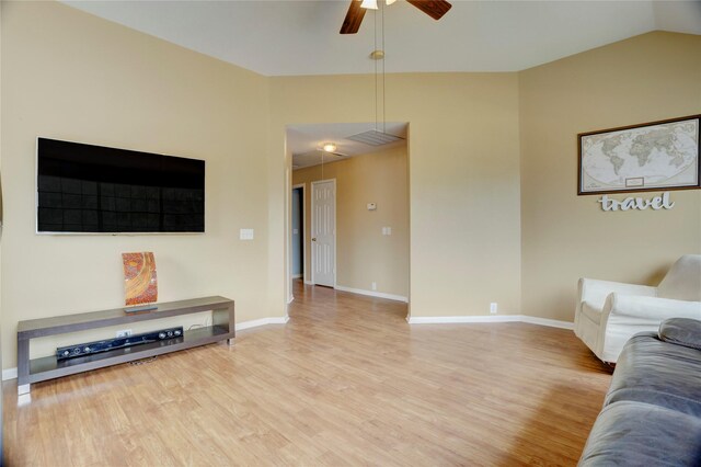 living area with attic access, a ceiling fan, baseboards, light wood-type flooring, and vaulted ceiling