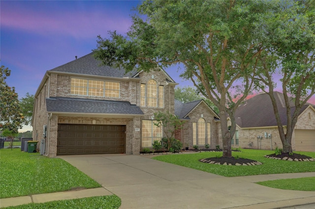 traditional home with concrete driveway, brick siding, a shingled roof, and a front lawn
