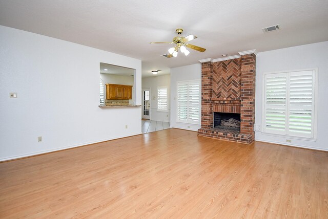 unfurnished living room with ceiling fan, visible vents, a brick fireplace, baseboards, and light wood finished floors