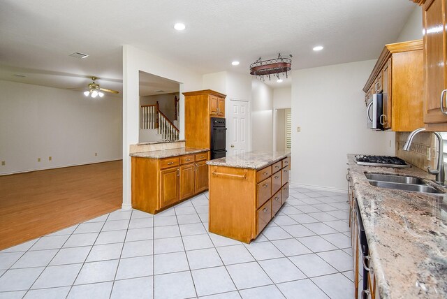 kitchen featuring a ceiling fan, brown cabinetry, a sink, and a center island