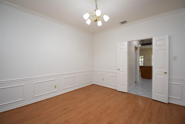 unfurnished room featuring visible vents, crown molding, wood finished floors, a wainscoted wall, and a chandelier