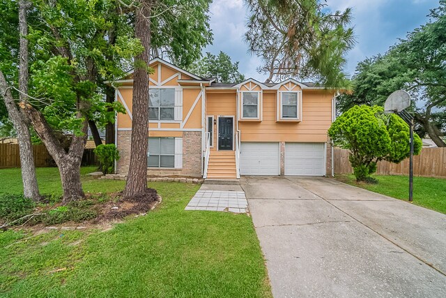 raised ranch with a garage, fence, a front yard, brick siding, and driveway