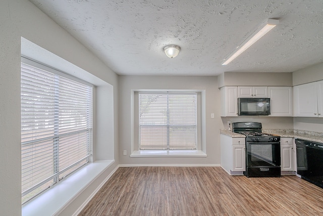 kitchen with white cabinets, light wood-style floors, a textured ceiling, baseboards, and black appliances