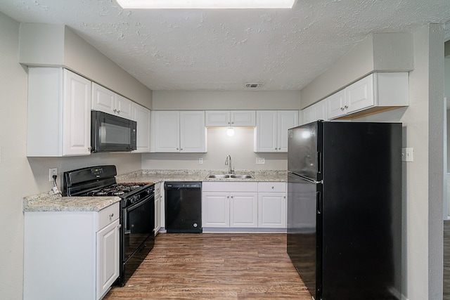 kitchen with dark wood-style flooring, a sink, a textured ceiling, visible vents, and black appliances
