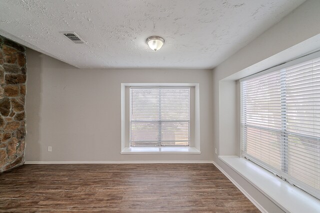 spare room featuring baseboards, dark wood finished floors, a textured ceiling, and visible vents