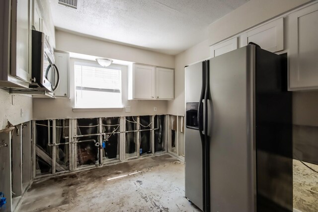 kitchen featuring visible vents, a textured ceiling, white cabinets, unfinished concrete flooring, and appliances with stainless steel finishes