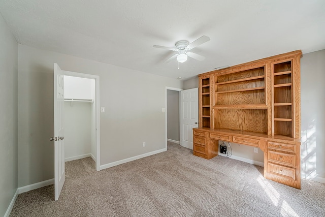 unfurnished bedroom featuring a closet, baseboards, a walk in closet, ceiling fan, and light colored carpet
