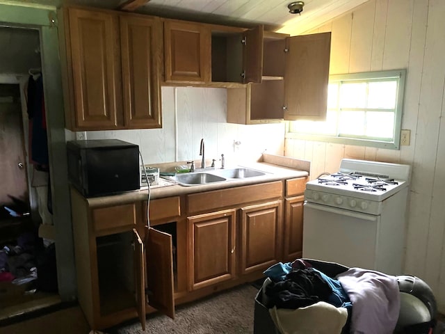 kitchen featuring brown cabinetry, a sink, light countertops, white range with gas cooktop, and wooden walls