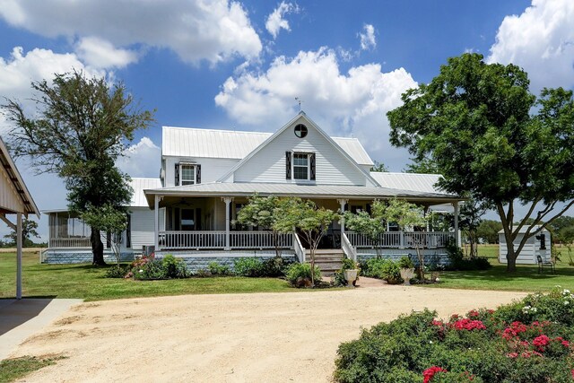farmhouse with covered porch, metal roof, and a front yard