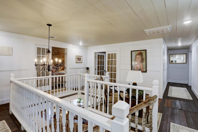 corridor featuring wood ceiling, dark wood-style flooring, visible vents, a notable chandelier, and an upstairs landing