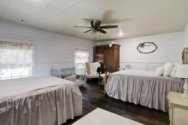 bedroom featuring visible vents, a ceiling fan, wooden walls, and dark wood-style floors