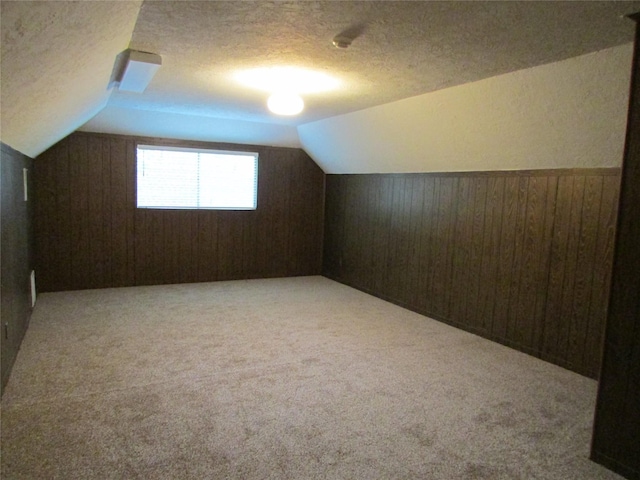bonus room with a textured ceiling, lofted ceiling, wooden walls, and light carpet