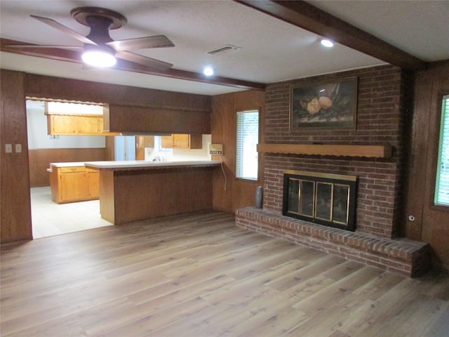 unfurnished living room featuring visible vents, wood walls, beamed ceiling, a ceiling fan, and light wood finished floors