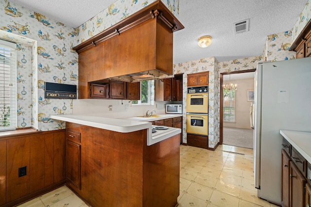 kitchen featuring a textured ceiling, visible vents, a peninsula, wallpapered walls, and white appliances