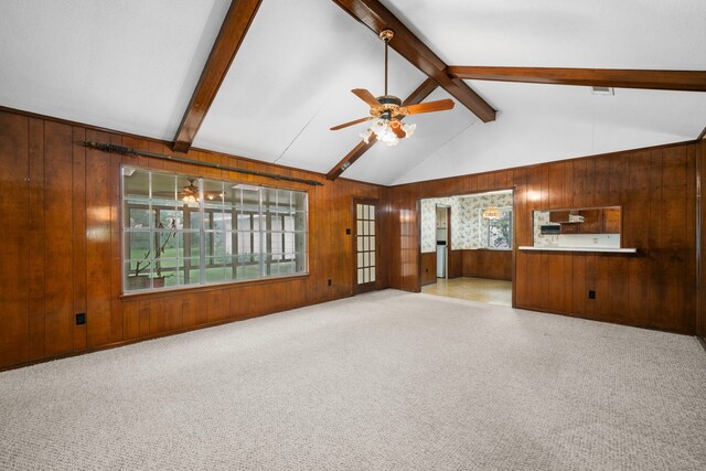 unfurnished living room featuring visible vents, ceiling fan, wooden walls, vaulted ceiling with beams, and carpet flooring