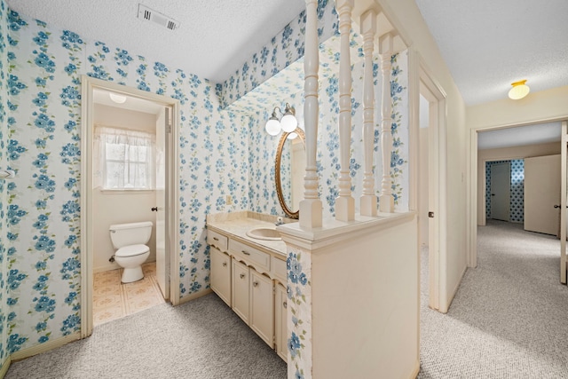 bathroom featuring a textured ceiling, visible vents, and wallpapered walls