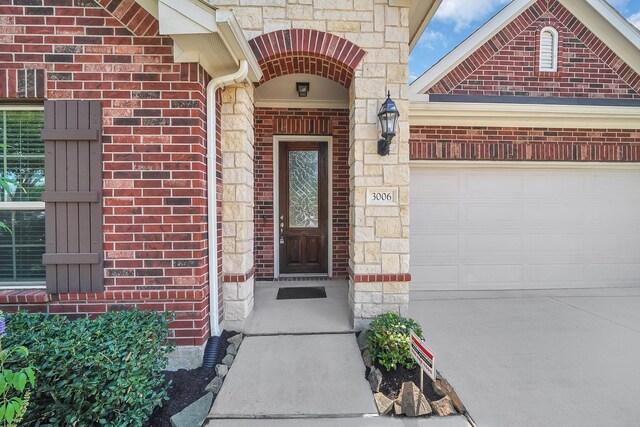 view of exterior entry with concrete driveway, brick siding, an attached garage, and stone siding