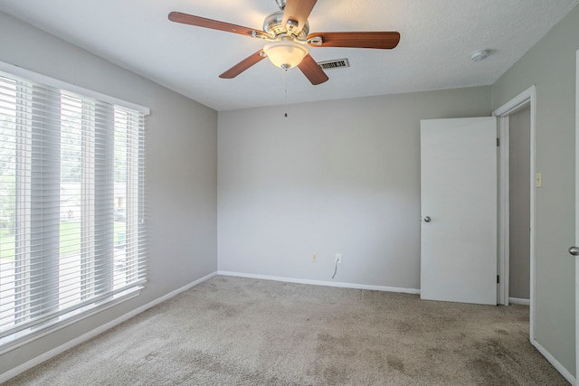carpeted empty room with visible vents, a ceiling fan, and baseboards
