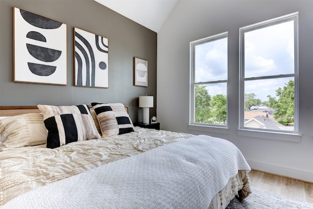 bedroom featuring baseboards, wood finished floors, and lofted ceiling