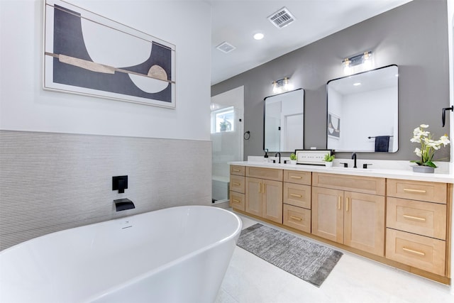 full bathroom featuring visible vents, double vanity, a freestanding bath, tile patterned floors, and a sink