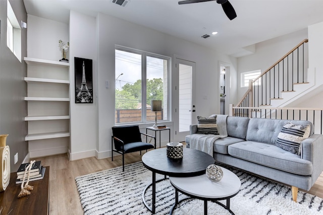 living area with visible vents, baseboards, ceiling fan, stairway, and light wood-type flooring