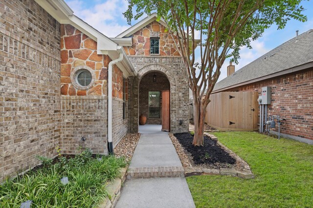 view of exterior entry featuring fence, a lawn, brick siding, and stone siding