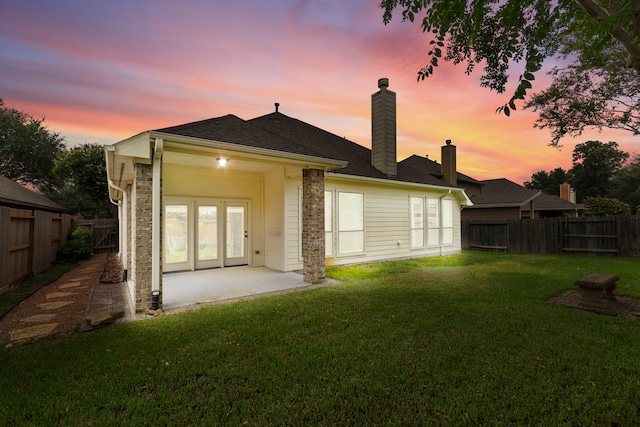 back of house with a chimney, roof with shingles, a patio area, a fenced backyard, and a yard