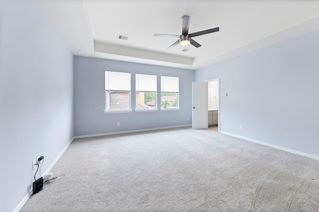 empty room with a tray ceiling, visible vents, ceiling fan, and carpet