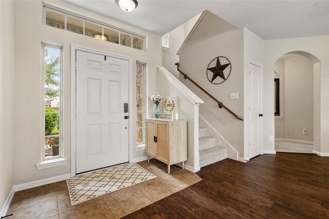 foyer featuring arched walkways, baseboards, stairs, and dark wood-style floors