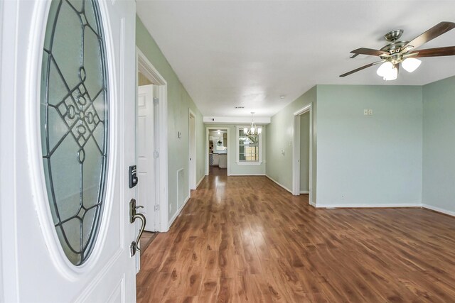 foyer with baseboards, wood finished floors, and ceiling fan with notable chandelier
