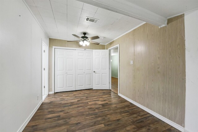 unfurnished bedroom with crown molding, wood walls, dark wood-style flooring, and visible vents