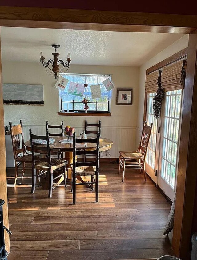 dining area with a wainscoted wall, an inviting chandelier, a wealth of natural light, and dark wood-type flooring