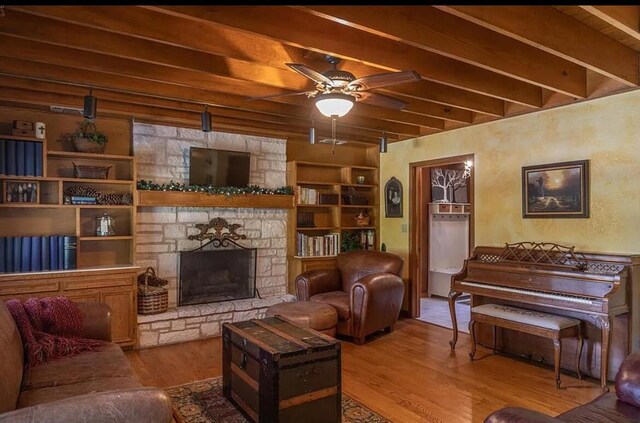 living area featuring wood finished floors, ceiling fan, beam ceiling, and a fireplace