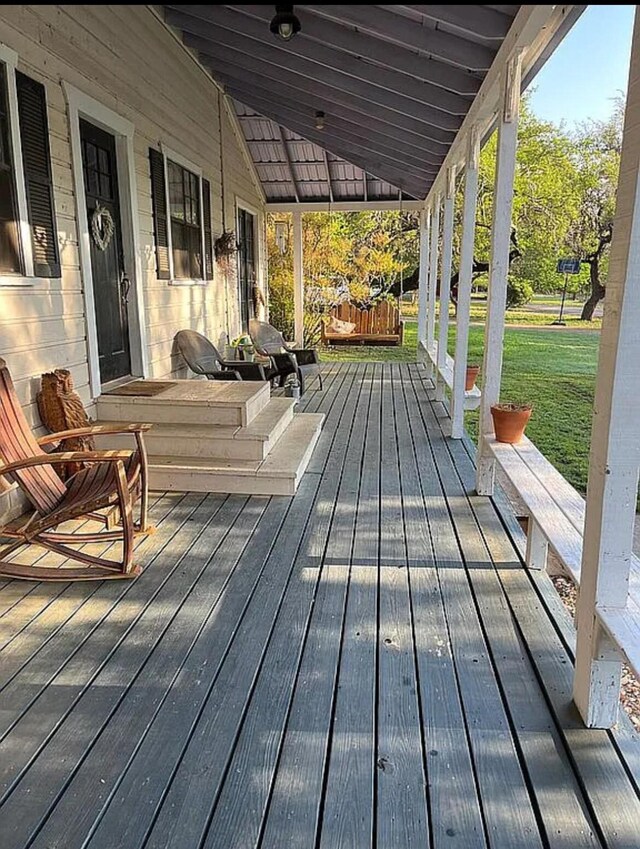 wooden terrace featuring a lawn and a porch