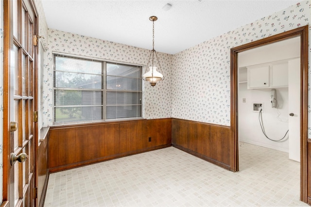605 N Rivershire Dr, Conroe, TX 77304 - unfurnished dining area featuring a textured ceiling, wallpapered walls, light floors, and a wainscoted wall