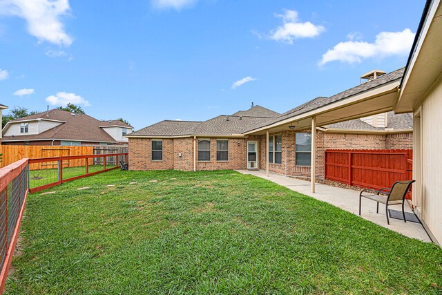 back of property with a fenced backyard, brick siding, a shingled roof, a patio area, and a yard