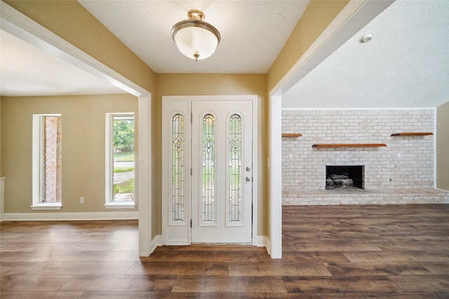 entrance foyer featuring wood finished floors, baseboards, and a brick fireplace