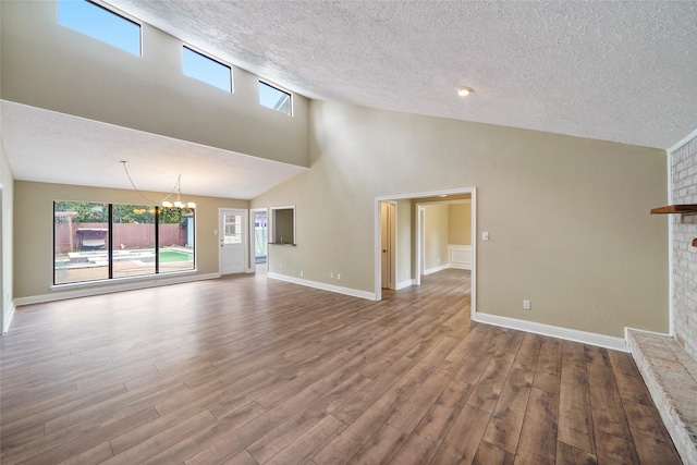 unfurnished living room with wood finished floors, a textured ceiling, high vaulted ceiling, a chandelier, and a fireplace