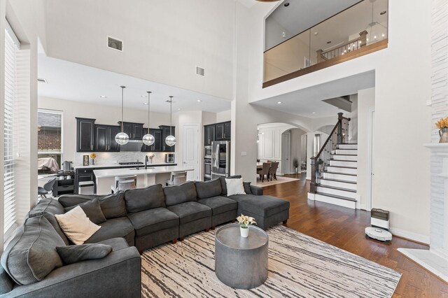 living room featuring dark wood-style flooring, a high ceiling, arched walkways, visible vents, and stairway
