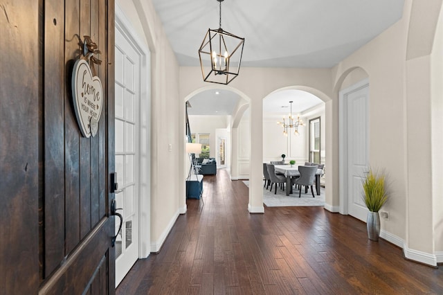 foyer entrance with arched walkways, baseboards, dark wood-type flooring, and a notable chandelier