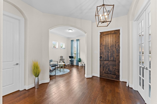 foyer entrance with arched walkways, baseboards, dark wood finished floors, and a chandelier