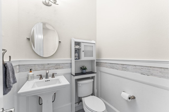 half bathroom featuring wainscoting and toilet