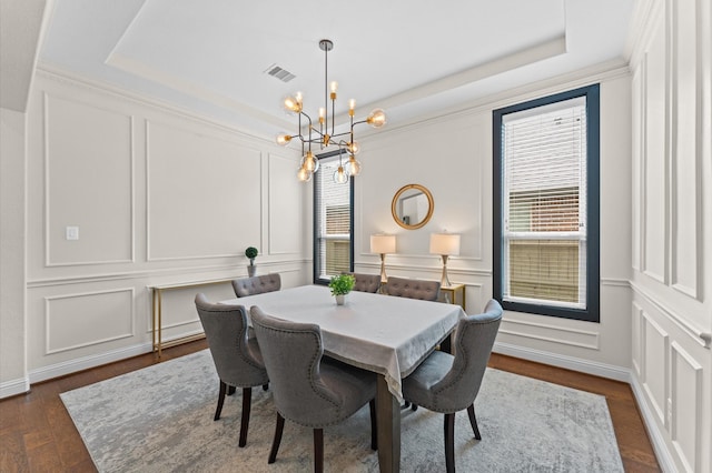 dining room featuring a decorative wall, a chandelier, a tray ceiling, visible vents, and dark wood-style floors