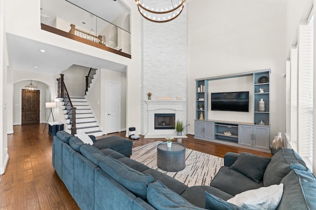 living room featuring an inviting chandelier, a towering ceiling, stairway, dark wood-type flooring, and arched walkways