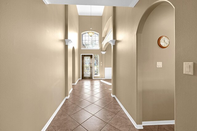 tiled entryway featuring baseboards, arched walkways, a textured wall, and a high ceiling