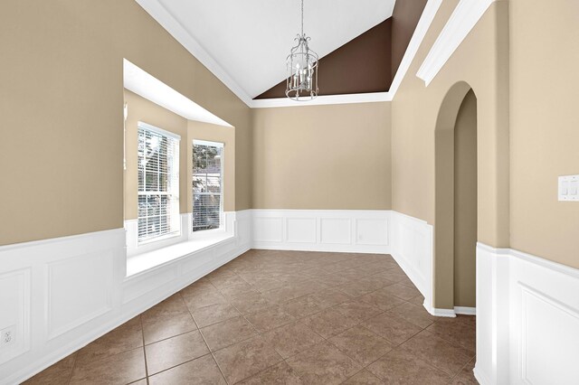 empty room featuring a wainscoted wall, arched walkways, a chandelier, and lofted ceiling