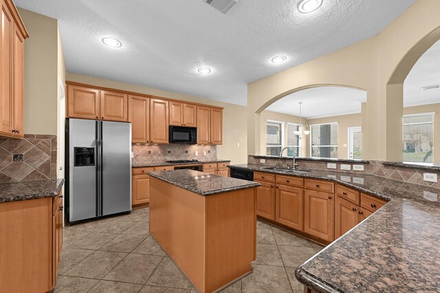 kitchen featuring arched walkways, decorative backsplash, a sink, and black appliances