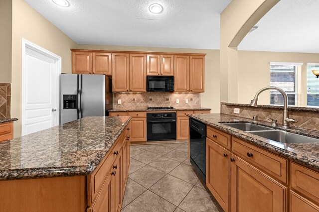 kitchen with dark stone countertops, a sink, black appliances, and tasteful backsplash