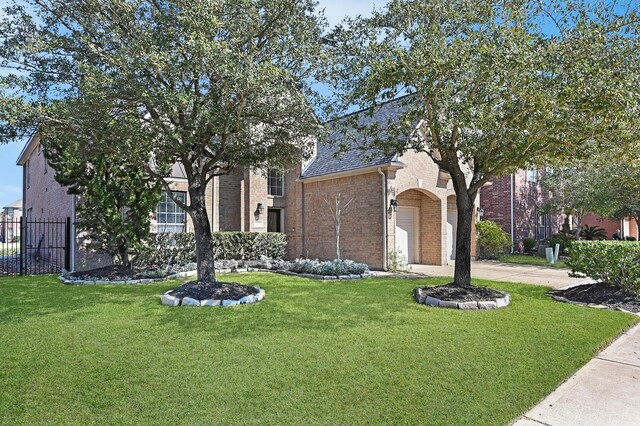 view of property hidden behind natural elements featuring brick siding, a front lawn, fence, and concrete driveway